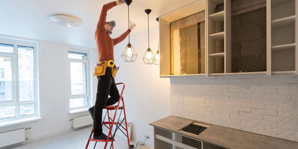 A craftsman hanging lights in the roof of a newly installed kitchen.