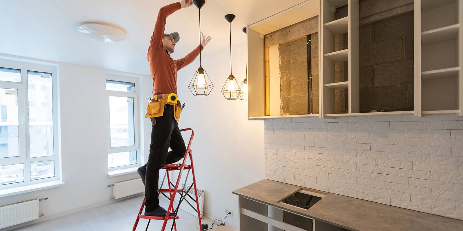 A craftsman hanging lights in the roof of a newly installed kitchen.